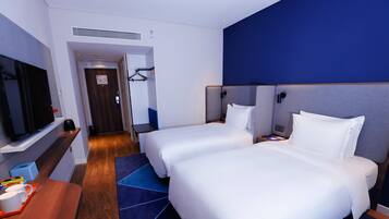 A hotel room with two beds, a TV, a desk with a tray of items, and a red chair.