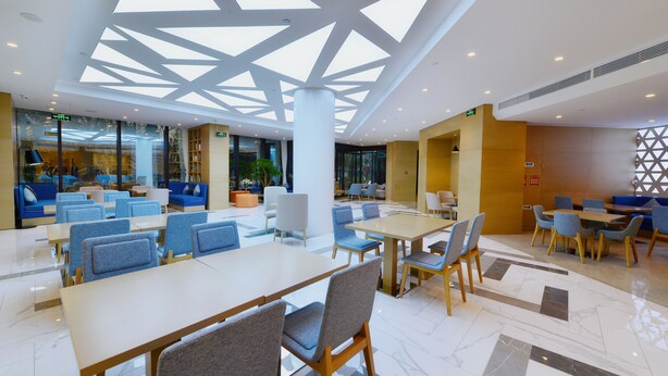 Un vaste espace intérieur aménagé avec différents types de sièges, notamment des tables et des chaises, et doté d’une grande verrière au plafond.