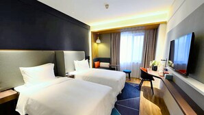 Une chambre d’hôtel avec deux lits, un bureau, une chaise, une télévision et une fenêtre avec des rideaux.