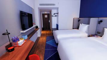 Habitación de hotel con televisión de pantalla plana, escritorio con cafetera, dos camas y alfombra azul.