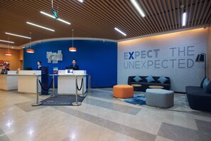 A hotel reception area with a blue wall, a sign that reads 'EXPECT THE UNEXPECTED', and a reception desk with two staff members. - Holiday Inn Express Tianshui City Center, an IHG Hotel (Tianshui)