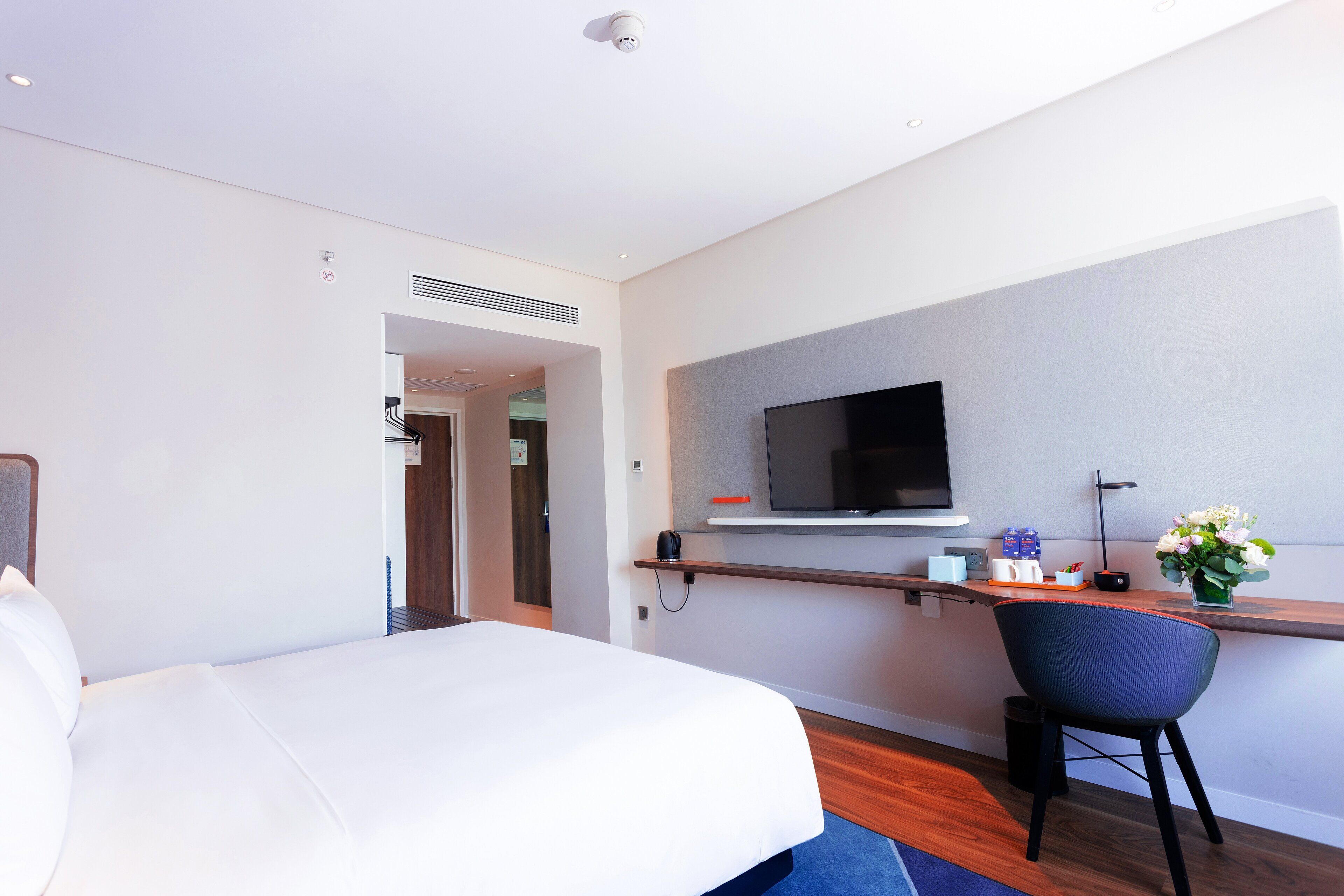 Habitación de hotel moderna con una cama, un escritorio con una silla, un televisor de pantalla plana y una pequeña mesa con un florero.