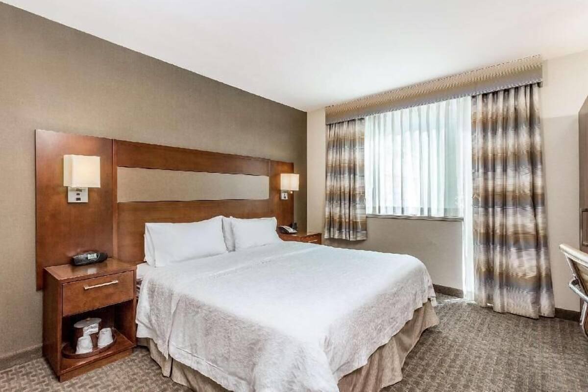 A hotel room with a large bed, bedside lamps, a nightstand, a desk, and a window with curtains.