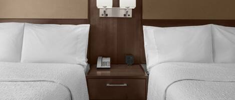 Una habitación de hotel con dos camas, una mesita de noche con un teléfono y una lámpara, y un cajón.