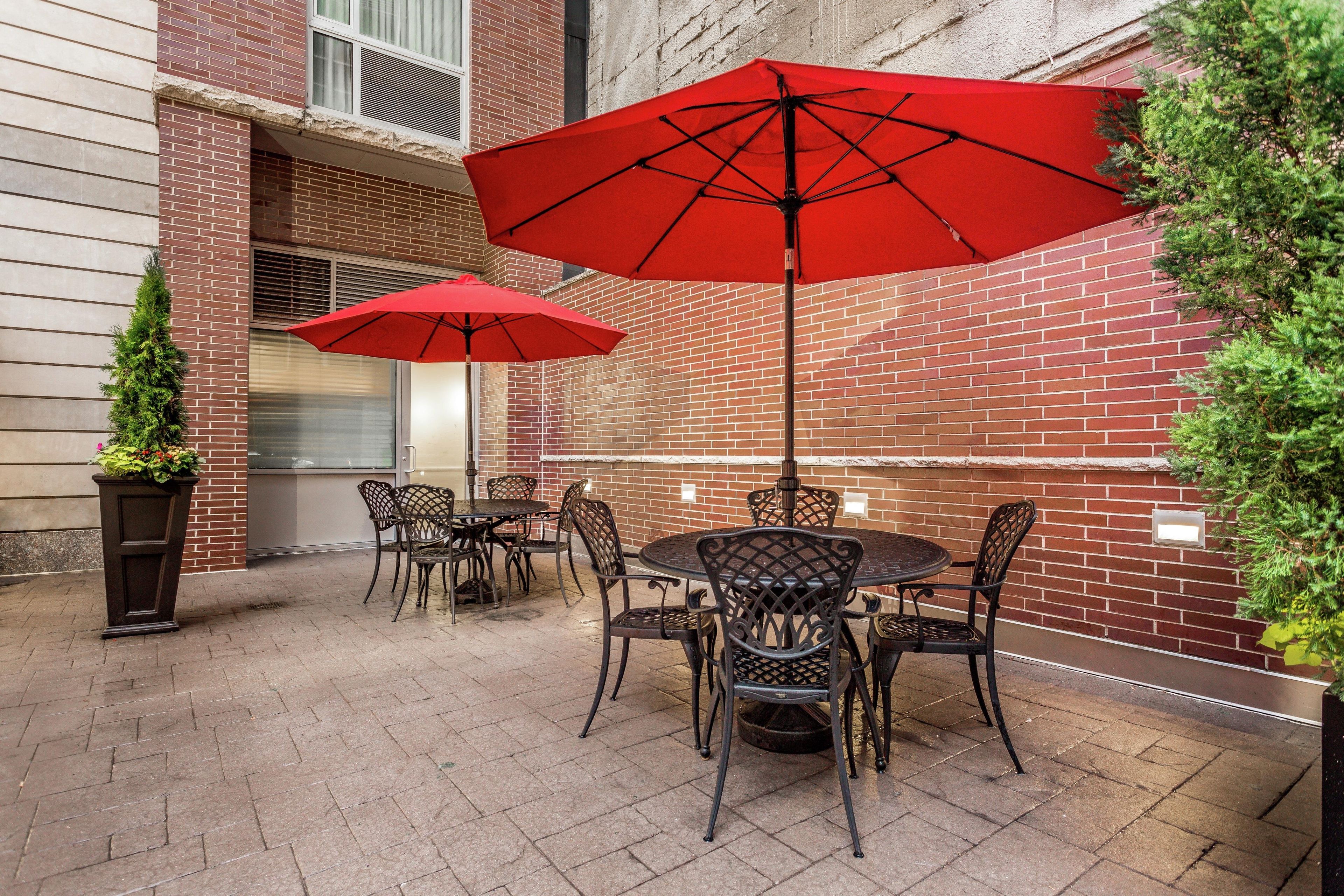 An outdoor patio with brick walls, metal chairs, and red umbrellas.