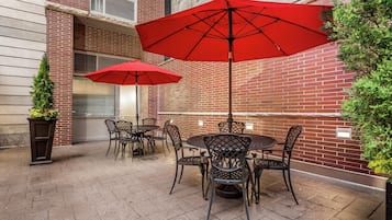 An outdoor patio with brick walls, metal chairs, and red umbrellas.
