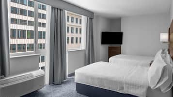 Habitación de hotel con una ventana grande, televisor de pantalla plana, cama con ropa blanca y una mesita de noche.