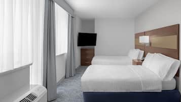 A hotel room with two beds, a flat-screen TV, a bedside table with a lamp, and a large window with curtains.