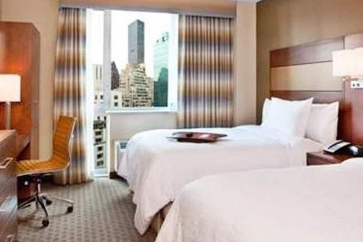 A hotel room with two beds, a desk, a chair, and a window with a city view.