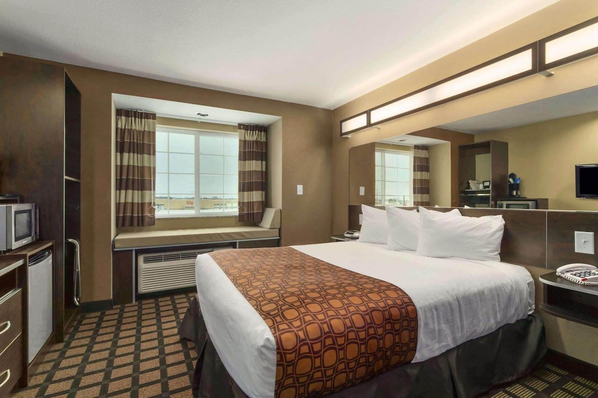 A hotel room with a bed, a desk, a television, and a window with curtains.