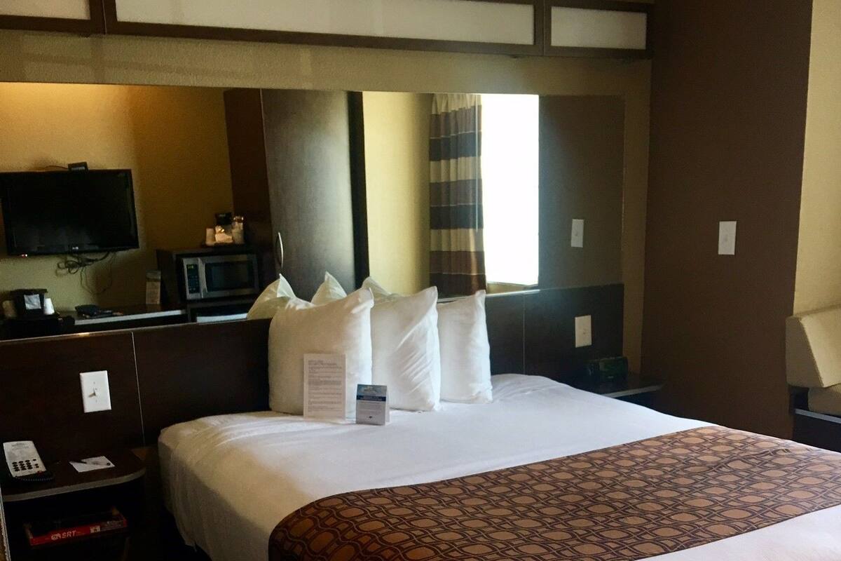 A hotel room with a large bed, a flat-screen TV, a microwave, and a bedside table with a phone and a box.