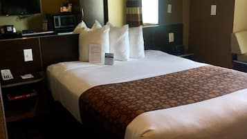 A hotel room with a large bed, a flat-screen TV, a microwave, and a bedside table with a phone and a box.