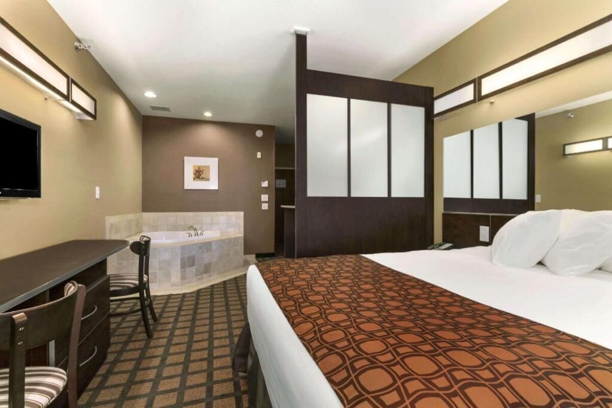 A hotel room with a bed, a desk, a chair, a bathroom with a bathtub, and a large mirror.