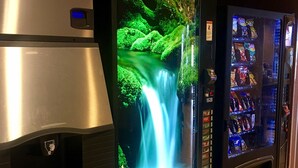 Una máquina expendedora con un expositor tipo cascada y un refrigerador.