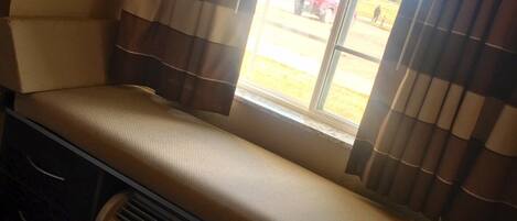 A small, cozy room with a bench seat by a window, a heater, and a view of the outside.
