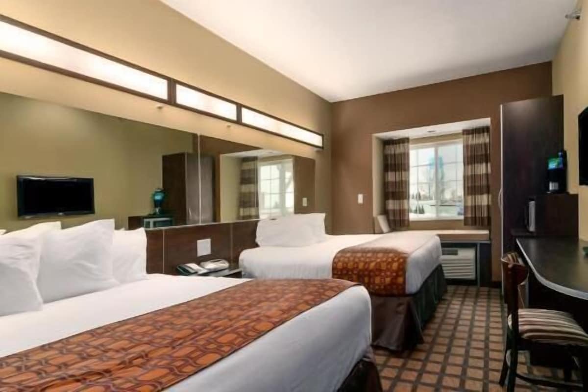 A hotel room with two beds, a TV, a desk, and a window with curtains.