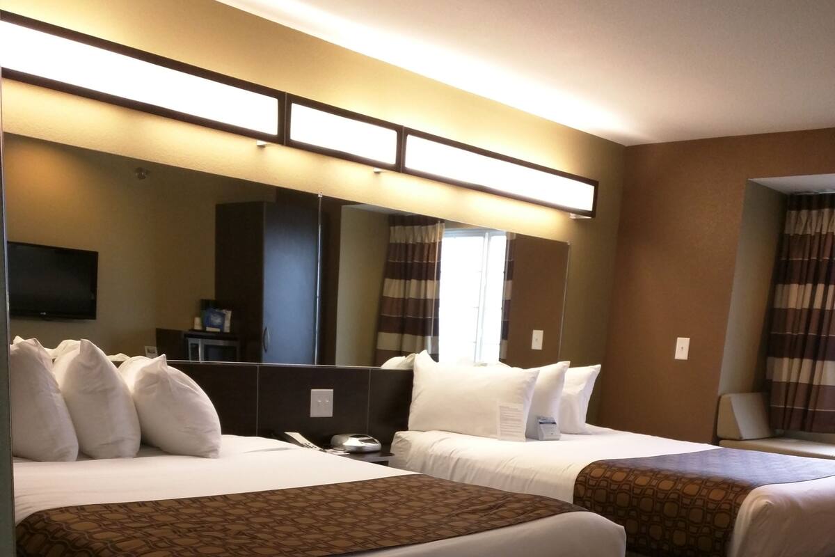 A hotel room with two beds, a flat-screen TV, a desk, and a large mirror.