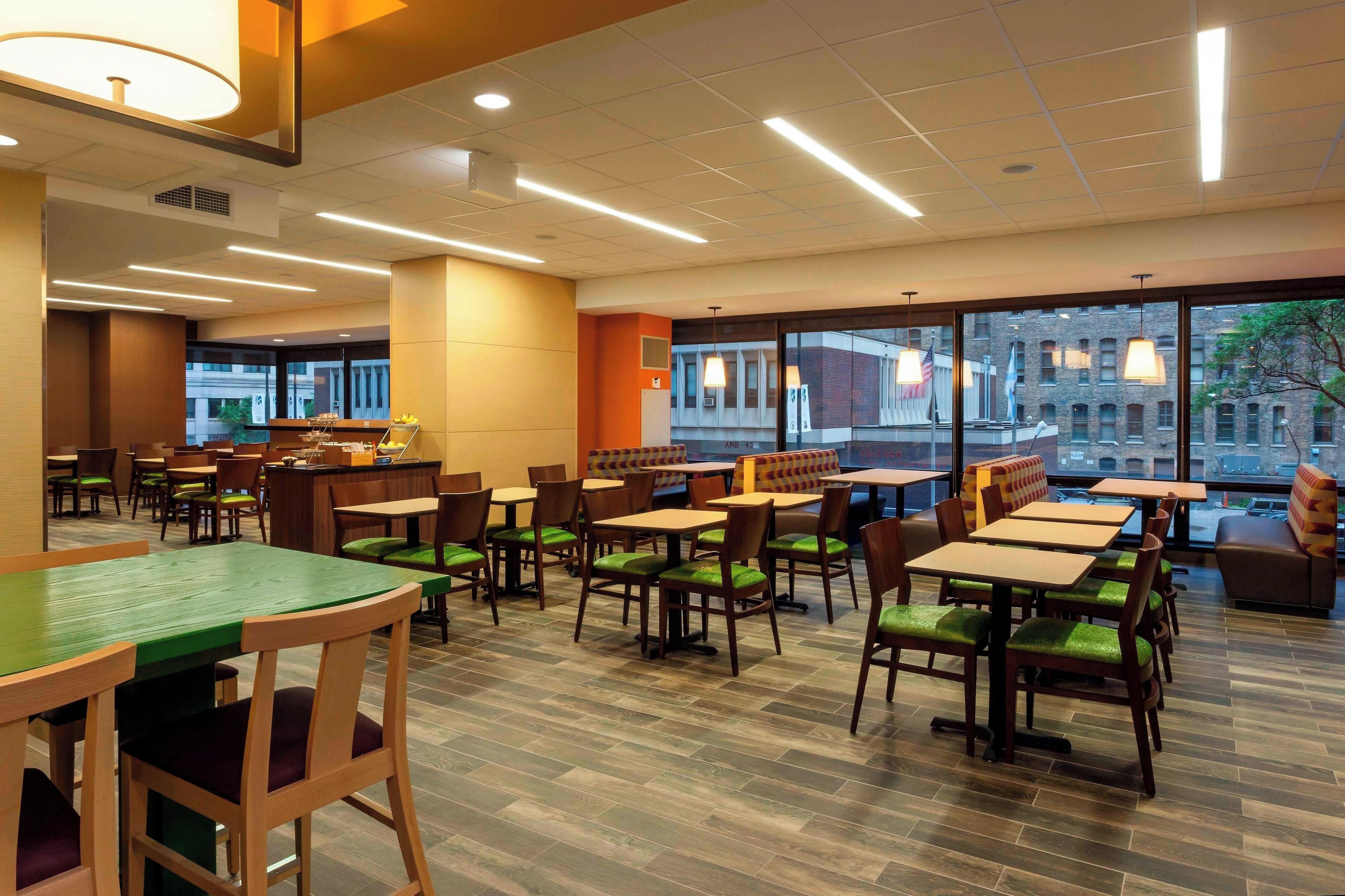 A restaurant with multiple tables and chairs, large windows, and a view of buildings outside.