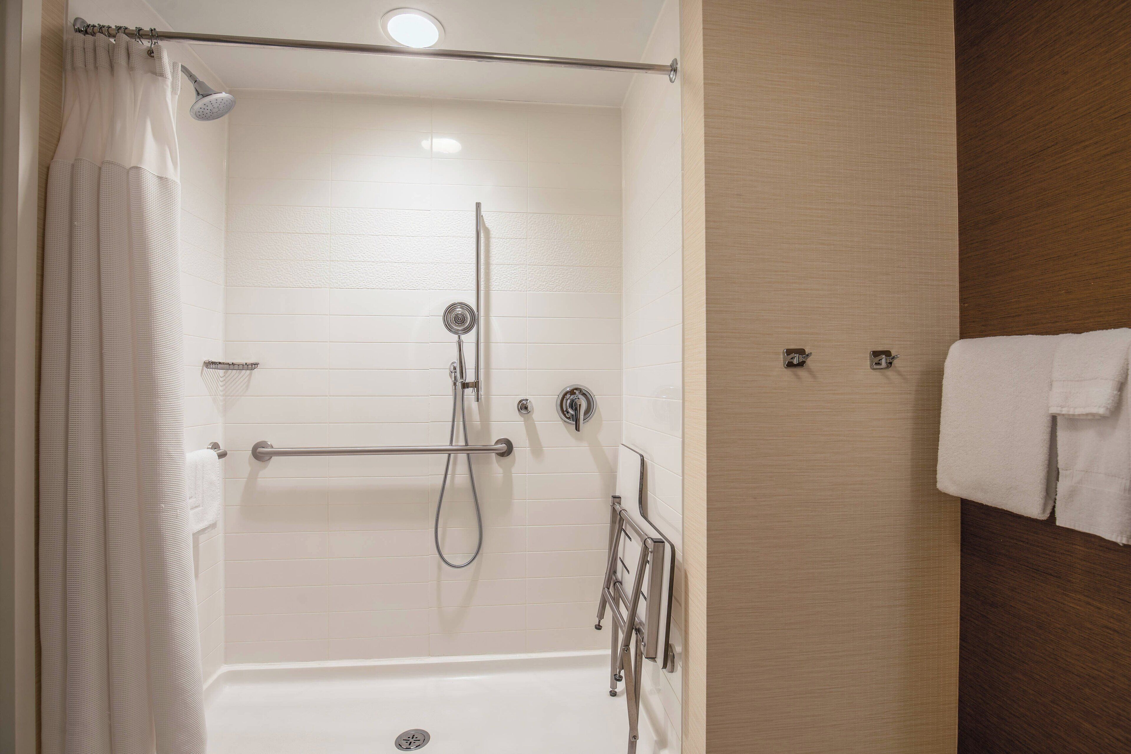 A walk-in shower with a grab bar, a handheld showerhead, and a towel rack.