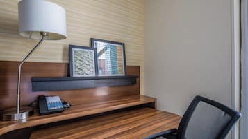 A hotel room with a wooden desk, a telephone, a lamp, and two framed artworks on the wall.