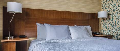 A hotel room with a wooden headboard, a bed with white bedding, two bedside tables, and a wall with a leaf pattern.