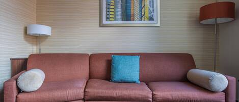Una sala de estar moderna con un sofá rojo, un cojín azul y un cuadro con una vista urbana enmarcada en la pared.