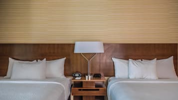 Quarto de hotel com duas camas, uma mesa de cabeceira com abajur e um relógio.