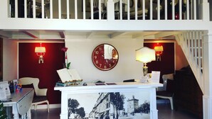 Zona de recepción con un mostrador, sillas, un reloj y una fotografía histórica enmarcada.