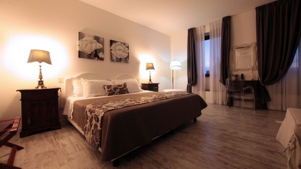 Una habitación de hotel con una cama grande, dos mesitas de noche con lámparas, un escritorio con silla y un espejo.