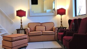 Una sala de estar con sofá, reposapiés y sillón, un espejo y dos lámparas.