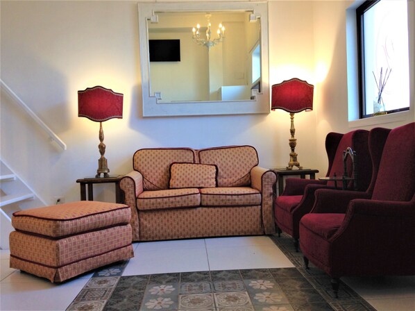 Ein Wohnzimmer mit Sofa, Hocker und Sesseln, einem Spiegel und zwei Lampen.