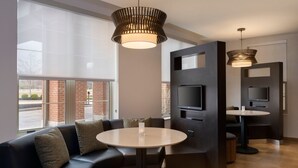 A modern hotel lobby with a sectional sofa, a round table, a flat-screen TV, and a large window offering a view of the outside. - Courtyard Columbus New Albany (New Albany)