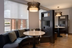 A modern hotel lobby with a sectional sofa, a round table, a flat-screen TV, and a large window offering a view of the outside.