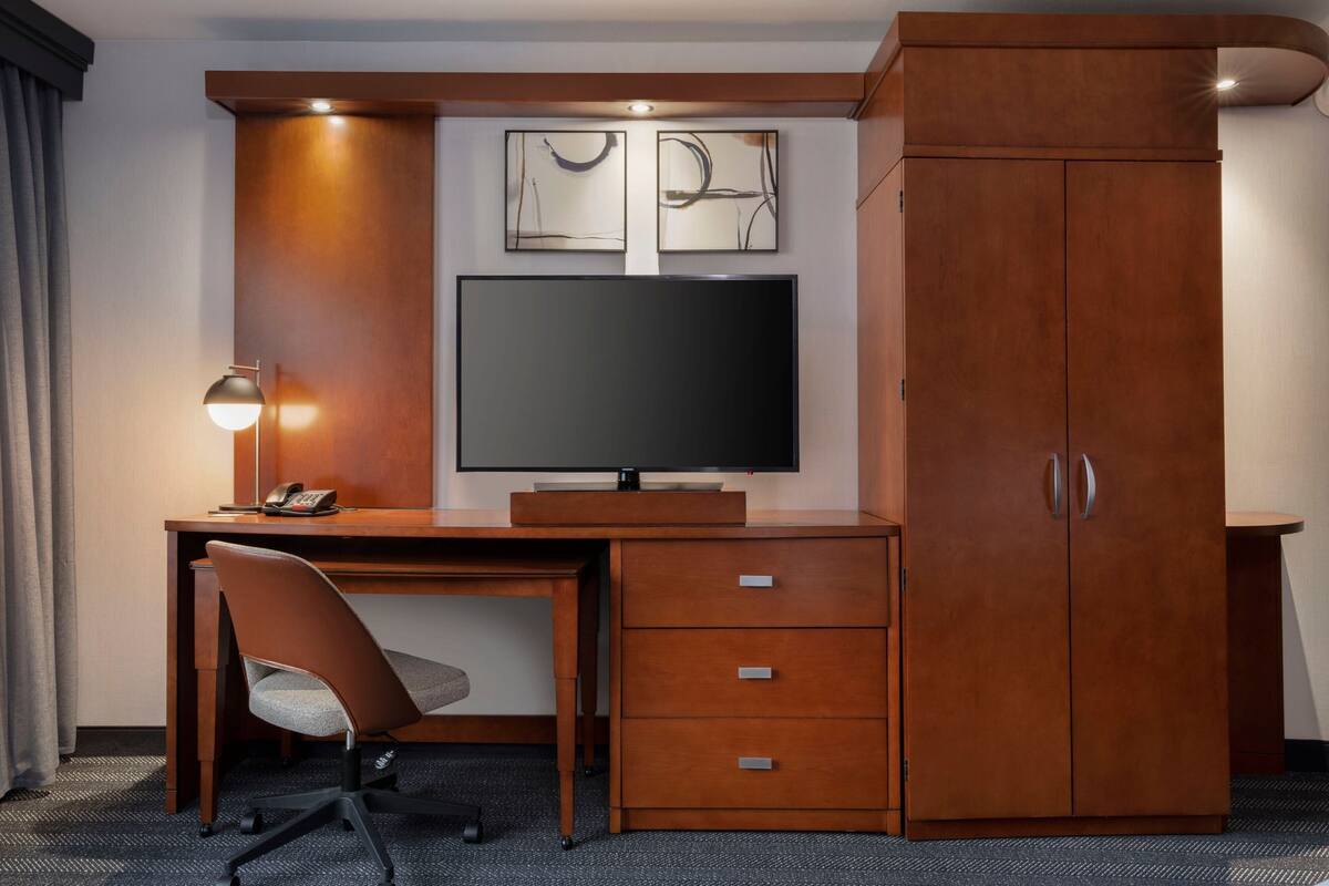 A hotel room with a wooden desk, a television, a chair, and a wardrobe.