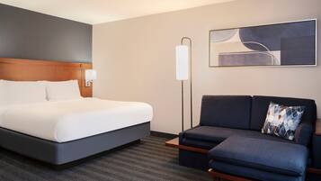 Une chambre d’hôtel avec un lit, un canapé, une lampe sur pied et un tableau au mur.