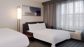 A hotel room with two beds, a standing lamp, a large window with curtains, and a wall-mounted air conditioner.