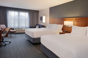 A hotel room with two beds, a desk, a chair, a lamp, and a window with curtains.