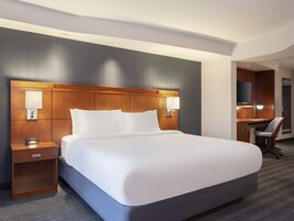 A hotel room with a large bed, bedside lamps, a desk with a chair, and a mirror.