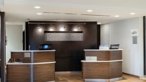 A modern hotel reception area with two reception desks, a digital screen, and a wall-mounted artwork. - Courtyard Columbus New Albany (New Albany)