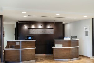 A modern hotel reception area with two reception desks, a digital screen, and a wall-mounted artwork.