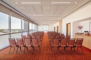 A conference room with rows of chairs, large windows, and a carpeted floor. - Courtyard by Marriott Leon at the Poliforum (León)
