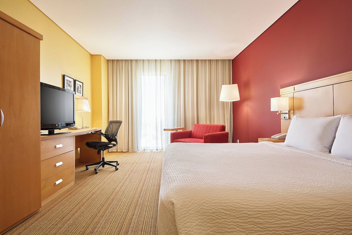A hotel room with a bed, a desk with a computer, a chair, a TV, and a lamp.