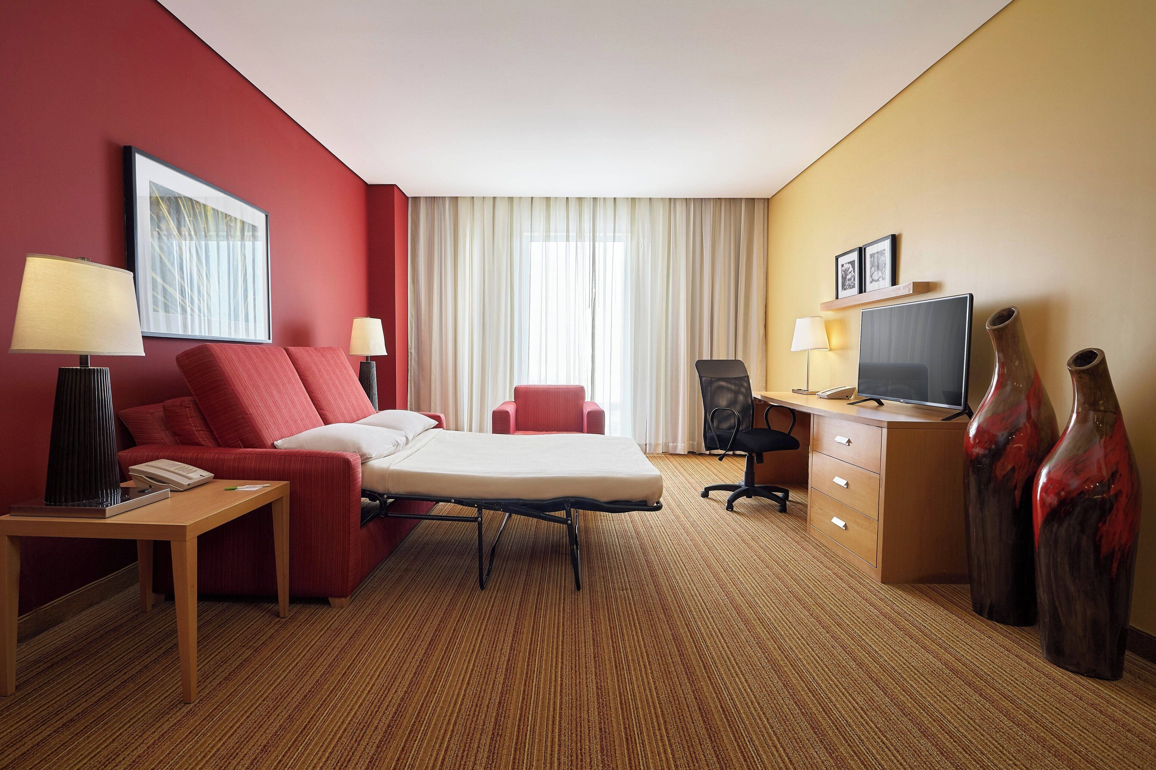 Une chambre d’hôtel comprenant un lit, un bureau avec un ordinateur, une chaise, une lampe et deux vases.