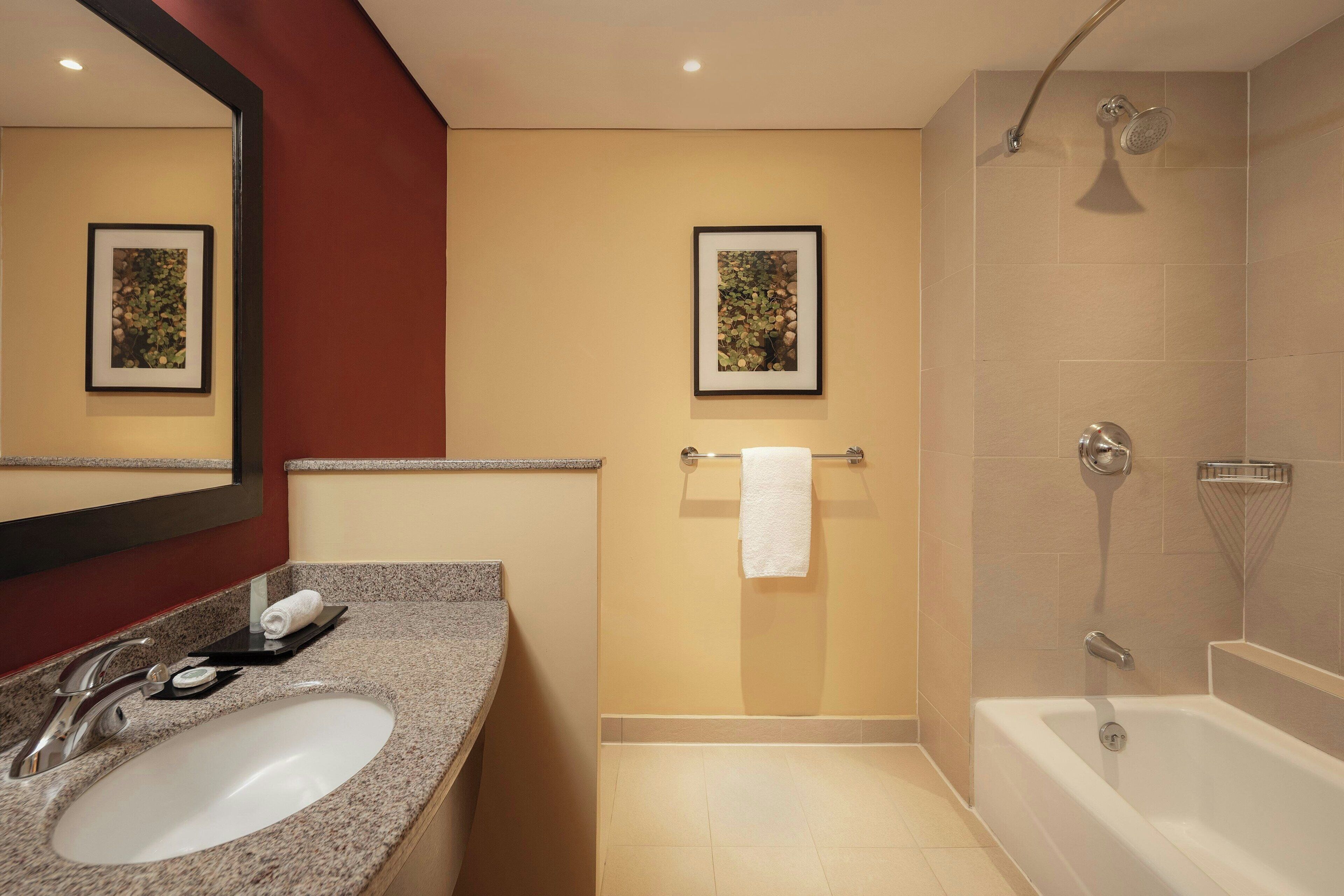 Un baño moderno con lavamanos de granito, un espejo grande, un cuadro en la pared, un perchero y una ducha a ras de suelo.