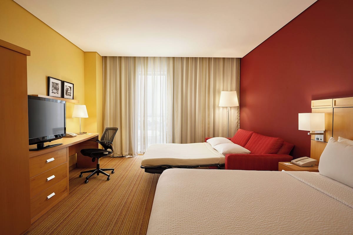 A hotel room with a bed, a desk with a computer, a chair, a TV, and a telephone.