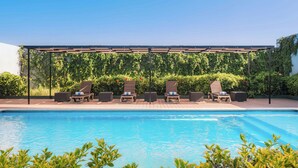 A poolside area with lounge chairs and a pergola. - Courtyard by Marriott Leon at the Poliforum (León)