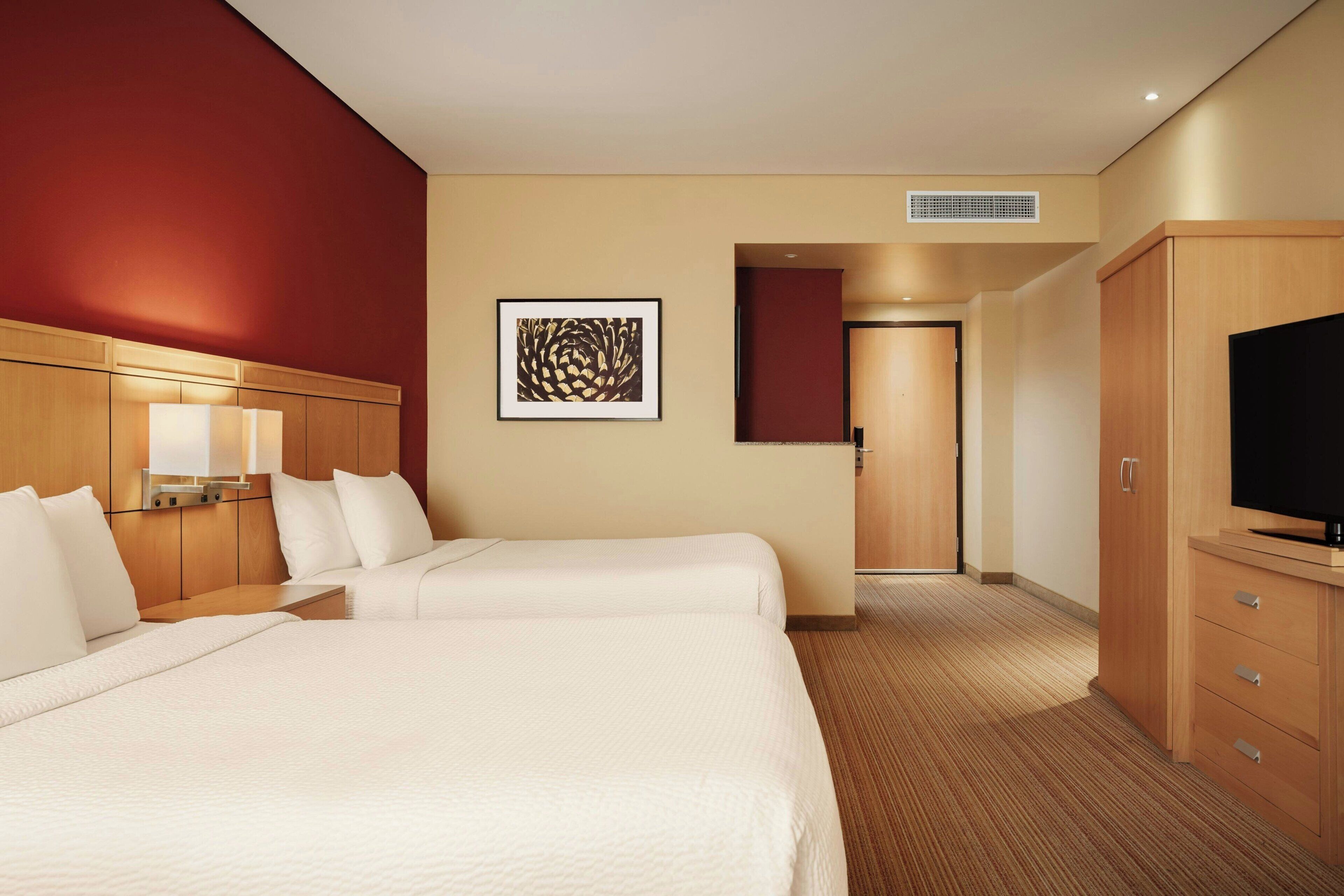 A hotel room with two beds, a TV, a desk, and a framed artwork on the wall.
