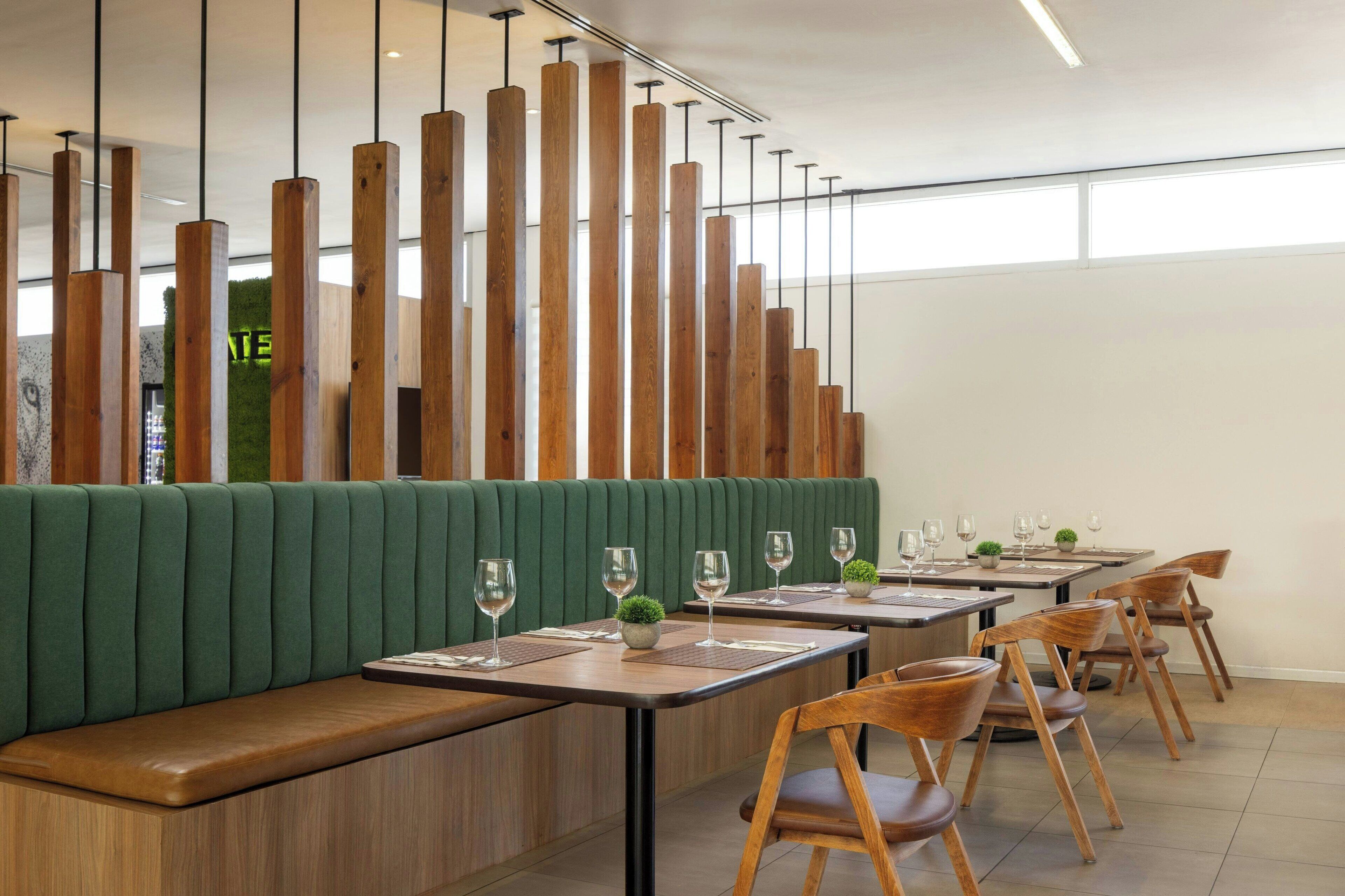 A restaurant interior with green upholstered booths, wooden tables, and chairs.