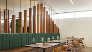 A restaurant interior with green upholstered booths, wooden tables, and chairs. - Courtyard by Marriott Leon at the Poliforum (León)