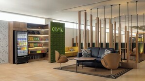 A modern lounge area with a seating arrangement, a refrigerator stocked with beverages, and a green wall with the word "CRATE". - Courtyard by Marriott Leon at the Poliforum (León)